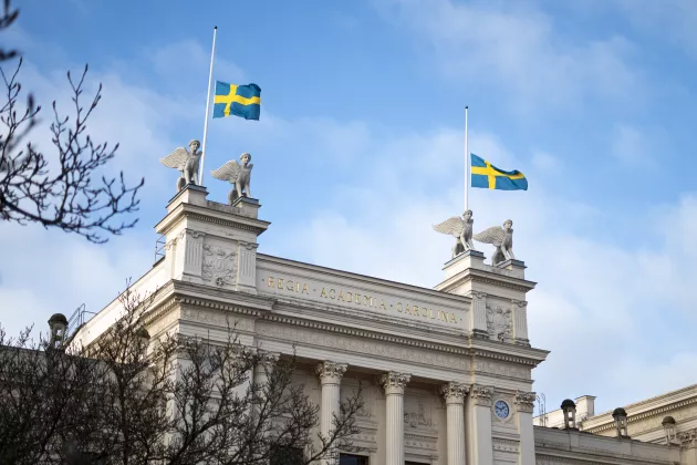 Foto på universitetshuset med två flaggor på halv stång.