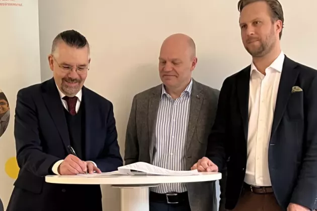 Three men in front of table signing a document.