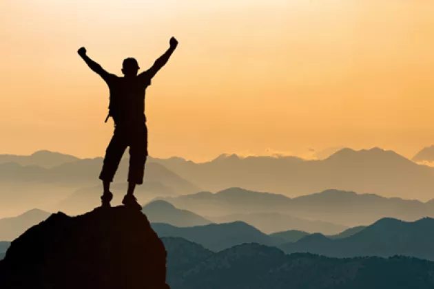 Man standing on a top of a mountain at sunset